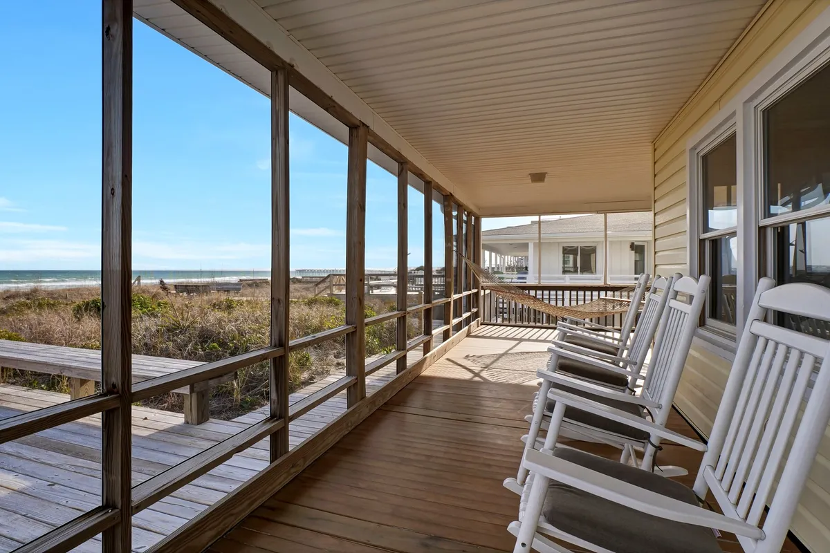 A serene exterior shot of an oceanfront deck featuring classic rocking chairs facing the open water. The wooden railing frames a breathtaking view of the ocean, inviting guests to relax, socialize, or enjoy the sunrise and sunset.