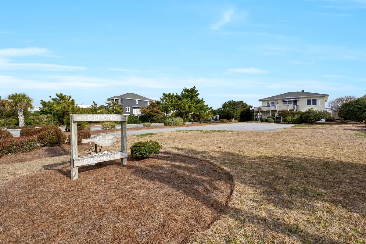 An exterior scene featuring a charming wooden sign surrounded by lush greenery and neighboring residential homes. The setting is relaxed and community-oriented, evoking a sense of exploration within the neighborhood and access to local amenities or preserves.